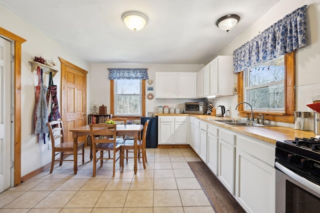 kitchen featuring white cabinetry, light tile patterned flooring, stainless steel range with gas stovetop, and a sink