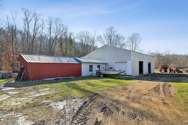 rear view of house with an outbuilding, a detached garage, dirt driveway, and metal roof