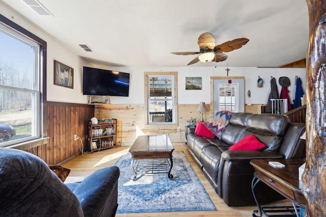 living area with visible vents, wood finished floors, wooden walls, wainscoting, and ceiling fan