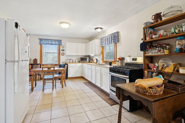 kitchen with stainless steel gas range oven, a wealth of natural light, light tile patterned floors, and freestanding refrigerator