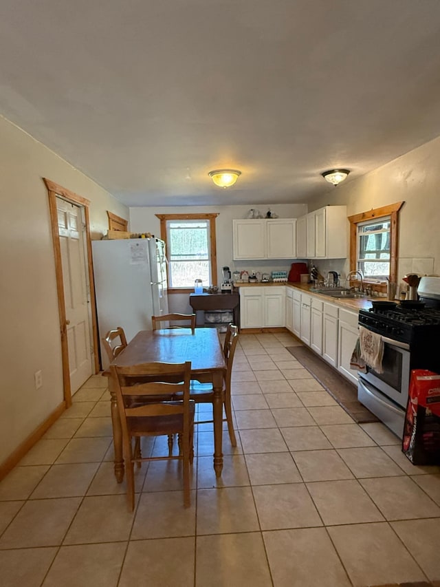 kitchen featuring stainless steel range with gas stovetop, freestanding refrigerator, light tile patterned flooring, white cabinetry, and a sink