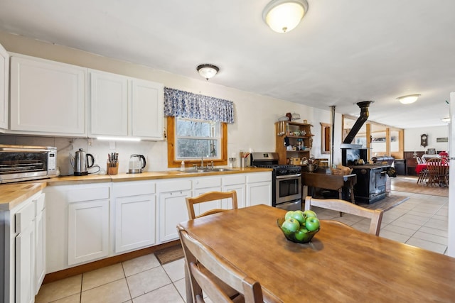 kitchen featuring light tile patterned floors, gas stove, a wood stove, a sink, and butcher block countertops