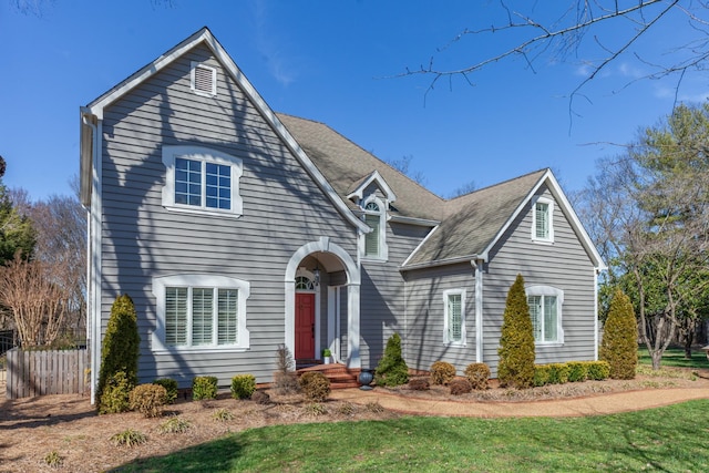 traditional-style home with a front lawn, fence, and roof with shingles