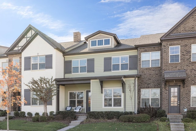 multi unit property with a front yard, brick siding, roof with shingles, and a chimney