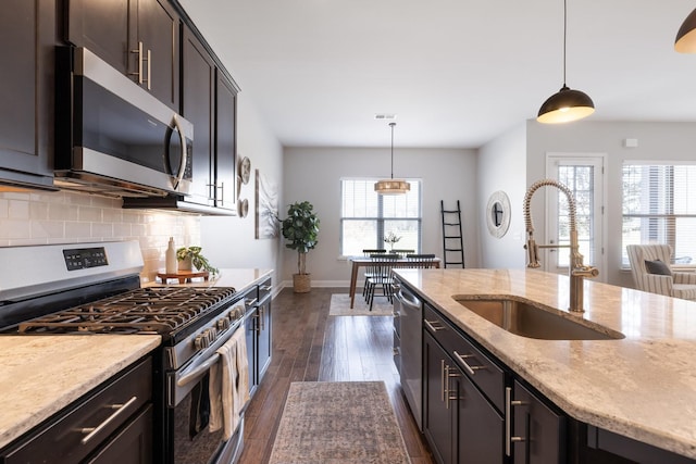 kitchen with backsplash, light stone countertops, dark wood finished floors, appliances with stainless steel finishes, and a sink