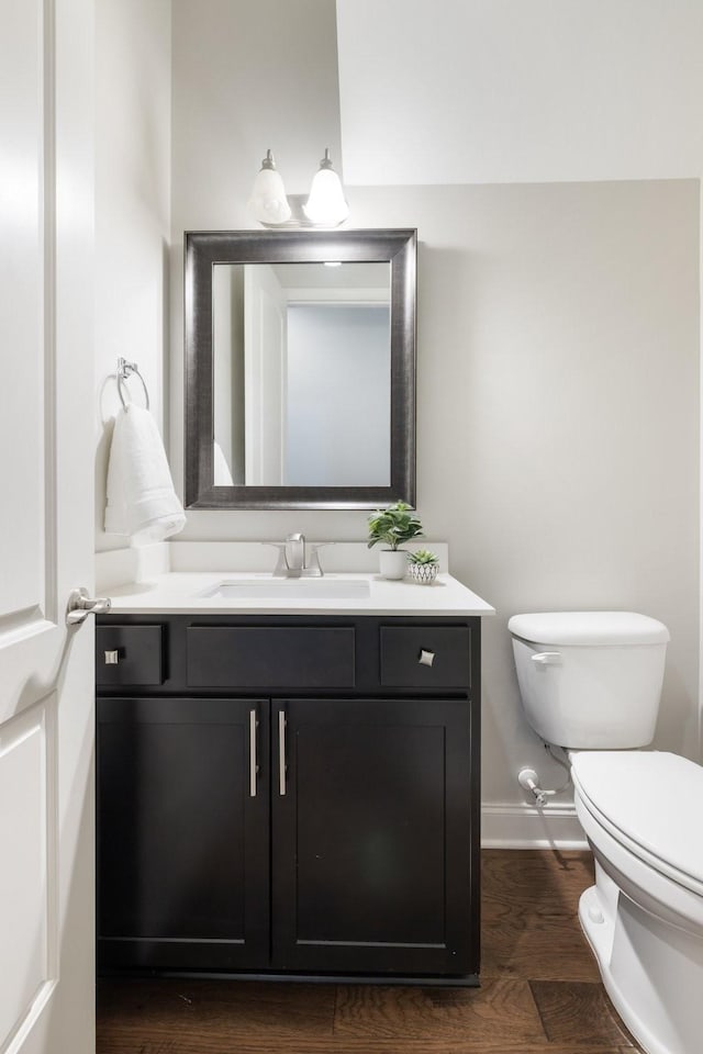 half bath with vanity, toilet, wood finished floors, and baseboards