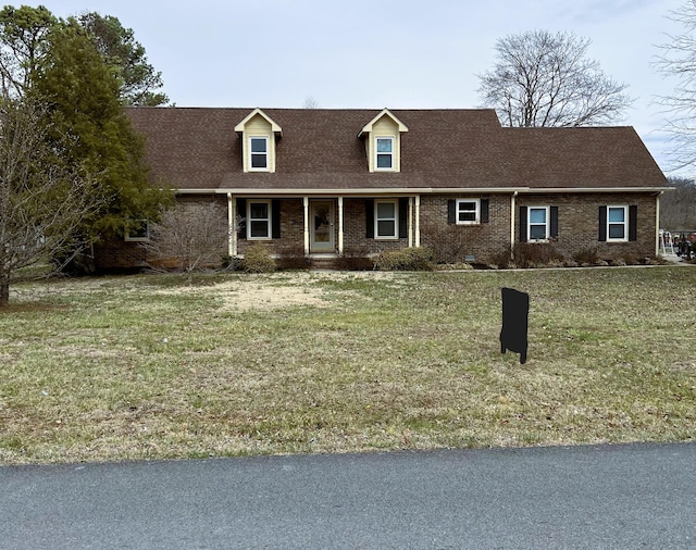 new england style home featuring a front lawn, brick siding, and roof with shingles