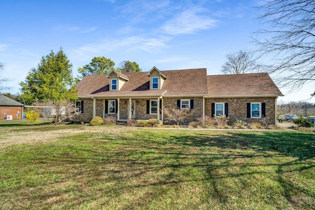 cape cod home featuring brick siding, a front lawn, and a shingled roof