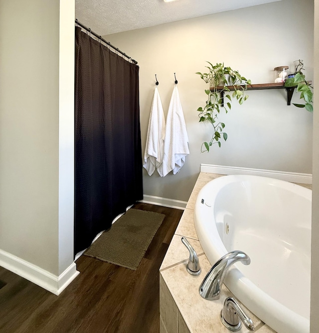 full bathroom featuring a garden tub, wood finished floors, baseboards, and a textured ceiling