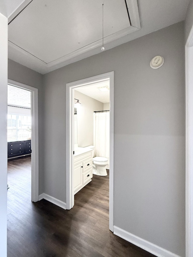 hallway featuring attic access, dark wood-type flooring, and baseboards