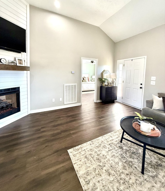 living area with visible vents, lofted ceiling, a large fireplace, and dark wood finished floors