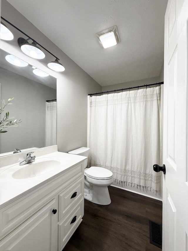 full bathroom featuring visible vents, toilet, a textured ceiling, wood finished floors, and vanity