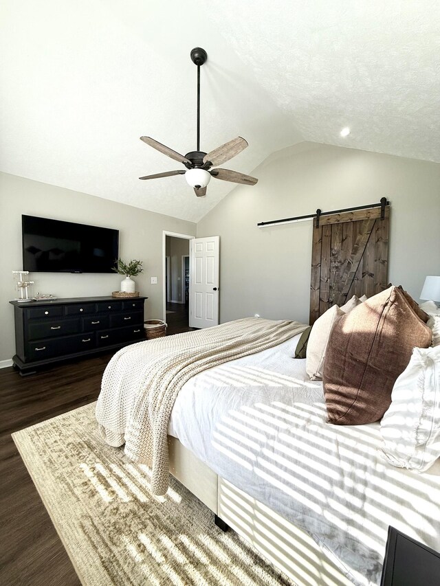 bedroom with dark wood-type flooring, ceiling fan, a barn door, vaulted ceiling, and a textured ceiling