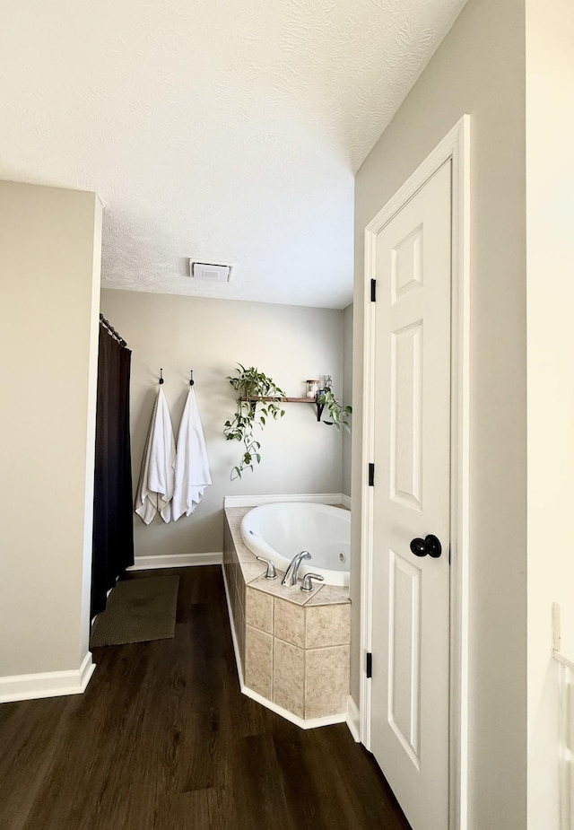 bathroom featuring visible vents, a textured ceiling, a tub with jets, and wood finished floors