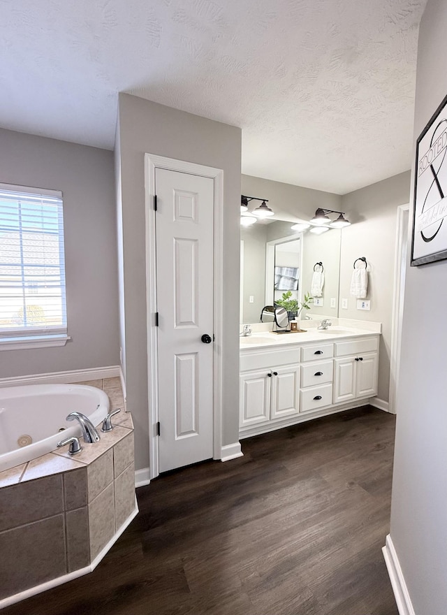 full bath with double vanity, a textured ceiling, wood finished floors, and a whirlpool tub