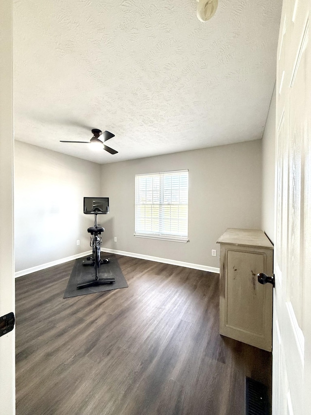 exercise area with baseboards, visible vents, ceiling fan, dark wood-type flooring, and a textured ceiling