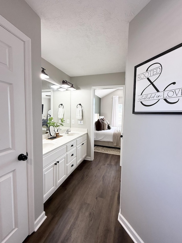 bathroom with double vanity, ensuite bathroom, wood finished floors, a textured ceiling, and a sink