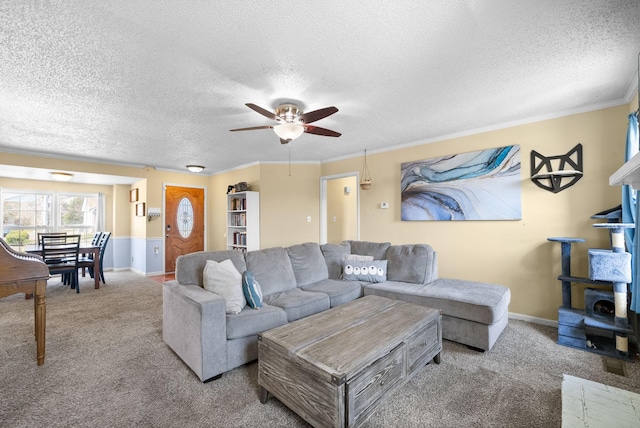 carpeted living room with ceiling fan, a textured ceiling, baseboards, and ornamental molding