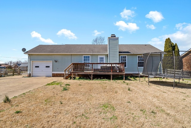 rear view of house with a deck, driveway, a trampoline, a garage, and a chimney