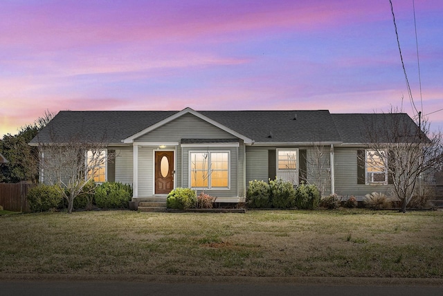 ranch-style house featuring cooling unit, a lawn, and a shingled roof