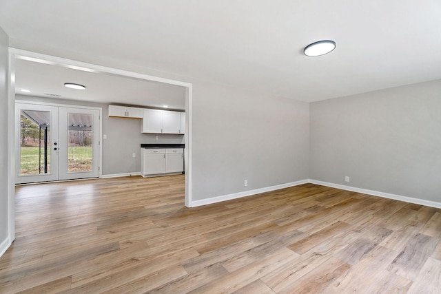 unfurnished living room with french doors, light wood-type flooring, and baseboards