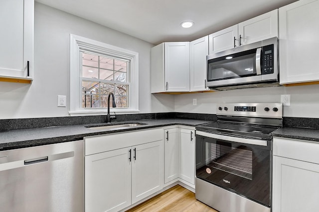 kitchen with a sink, stainless steel appliances, light wood-type flooring, and white cabinetry