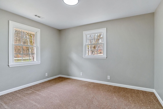 carpeted spare room featuring a wealth of natural light, visible vents, and baseboards