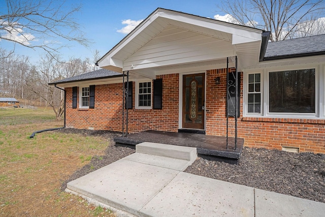 view of front facade featuring crawl space, covered porch, brick siding, and a shingled roof