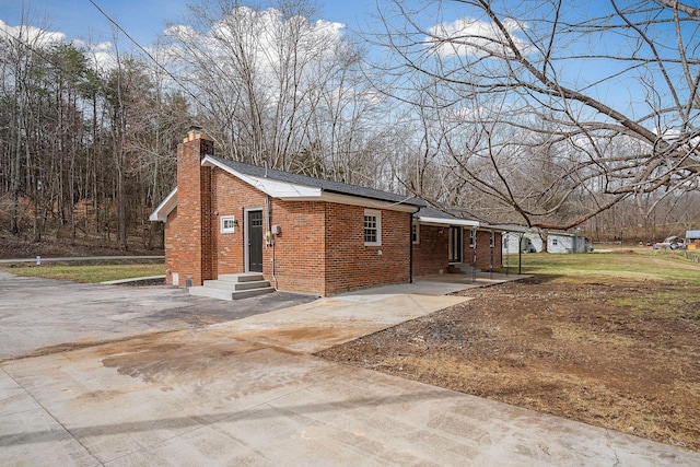 view of home's exterior with brick siding, a chimney, driveway, and entry steps