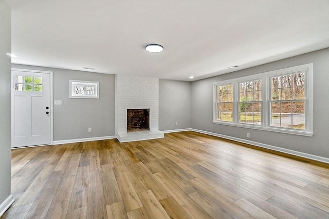 unfurnished living room with visible vents, baseboards, light wood-style floors, and a brick fireplace