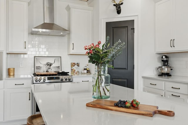 kitchen featuring wall chimney exhaust hood, light countertops, backsplash, and white cabinets