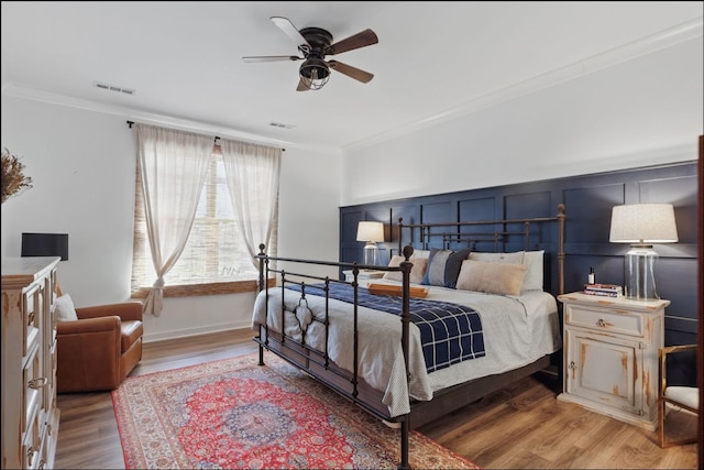 bedroom featuring ornamental molding, wood finished floors, a decorative wall, and ceiling fan