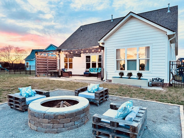 back of house at dusk with an outdoor living space with a fire pit, a patio, and roof with shingles