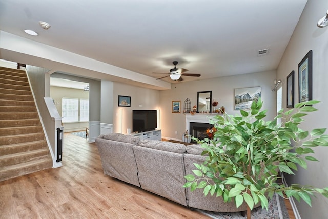 living area with light wood finished floors, visible vents, ceiling fan, stairs, and a fireplace