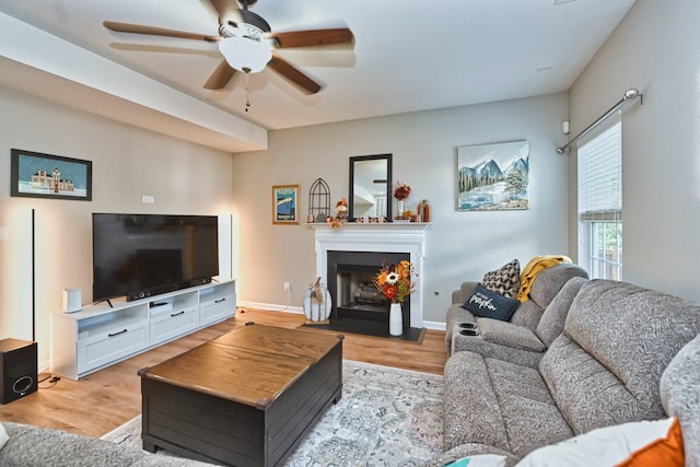 living room featuring light wood-style flooring, a fireplace with flush hearth, baseboards, and ceiling fan