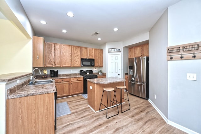 kitchen featuring light wood finished floors, a center island, a kitchen bar, black appliances, and a sink