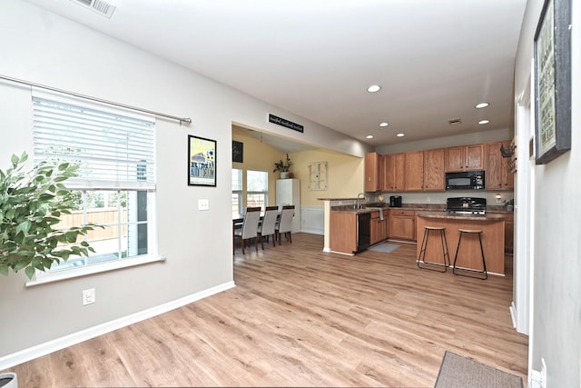 kitchen with black appliances, plenty of natural light, a peninsula, and light wood finished floors