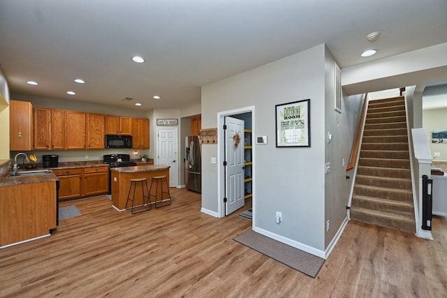 kitchen featuring light wood finished floors, black microwave, stainless steel refrigerator with ice dispenser, and a sink