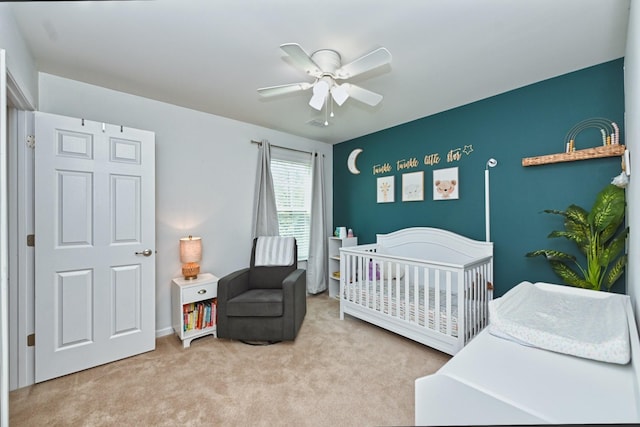 carpeted bedroom with a crib and ceiling fan