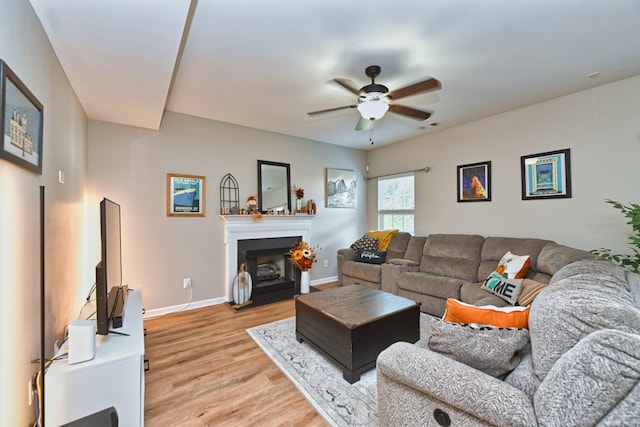 living room with light wood-type flooring, a fireplace with flush hearth, visible vents, a ceiling fan, and baseboards