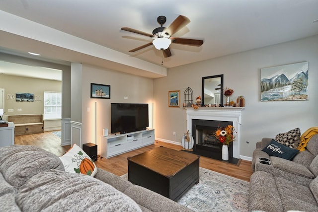 living room featuring a fireplace, wood finished floors, a wainscoted wall, and ceiling fan