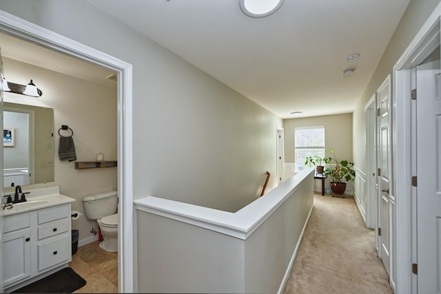 hallway with an upstairs landing, light carpet, baseboards, and a sink