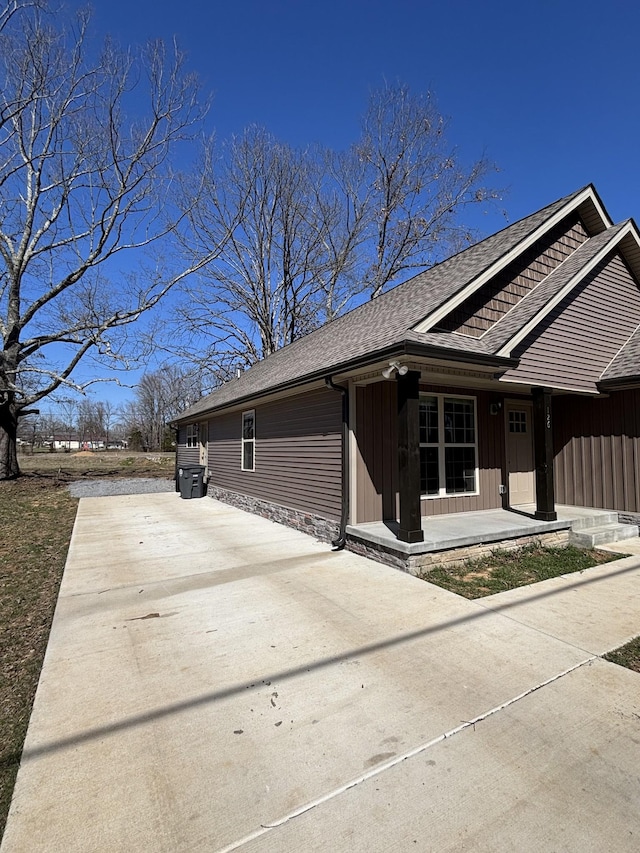 view of side of property with covered porch, board and batten siding, concrete driveway, and roof with shingles