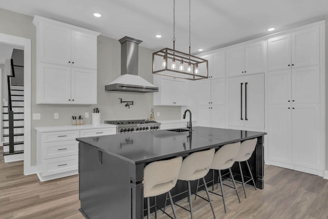 kitchen featuring a sink, light wood-style floors, a breakfast bar, and wall chimney exhaust hood