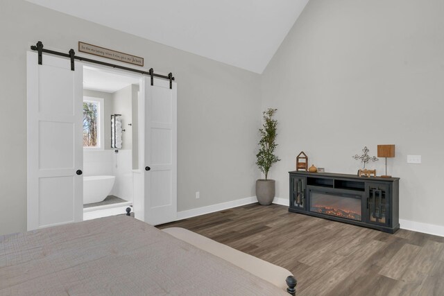 bedroom featuring a glass covered fireplace, vaulted ceiling, a barn door, and wood finished floors