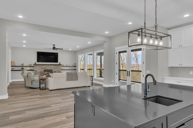 kitchen with light wood-style flooring, a sink, white cabinetry, recessed lighting, and a stone fireplace