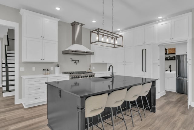 kitchen featuring light wood finished floors, wall chimney range hood, stainless steel appliances, white cabinetry, and a sink