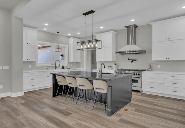 kitchen featuring wall chimney range hood, a center island with sink, a breakfast bar area, high end range, and a sink