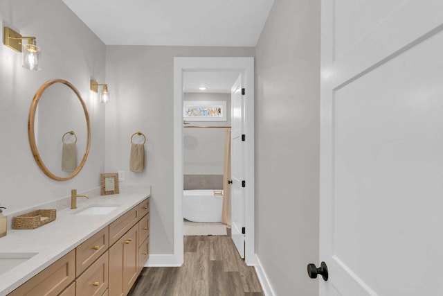 full bathroom featuring a freestanding tub, a sink, wood finished floors, double vanity, and baseboards