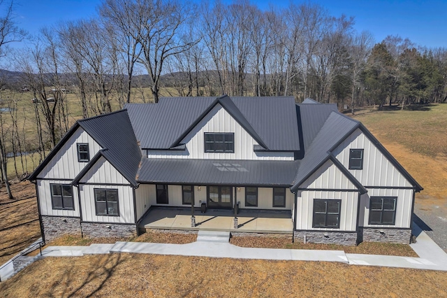 modern inspired farmhouse featuring stone siding, board and batten siding, metal roof, and a front yard